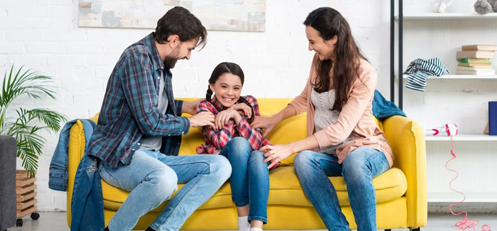 What We Offer: Family sitting on a yellow couch with their daughter.